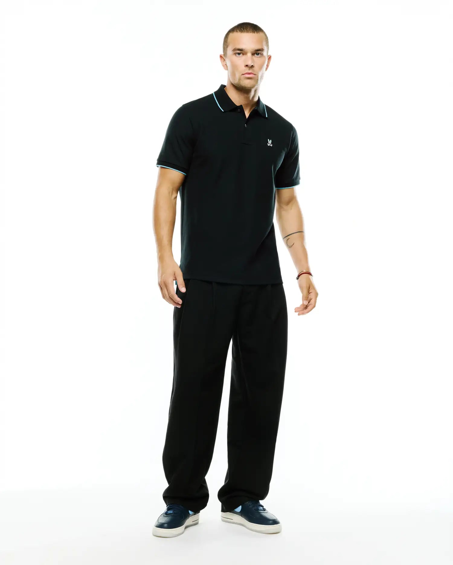 Men's Klaus Pique Polo, a classic fit black pique polo with light blue tipping on the collar and sleeve cuffs, featuring a small embroidered Psycho Bunny skull logo on the left chest. (4)
