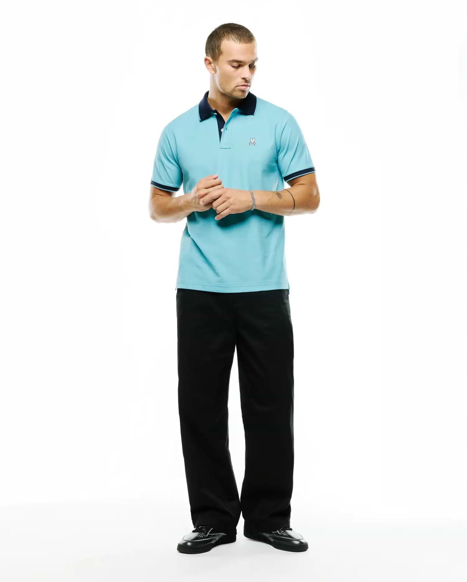 Men's Klaus Pique Polo in light blue, featuring a navy collar and cuffs with white trim. Small embroidered Psycho Bunny skull logo on the left chest. Classic fit. (4)