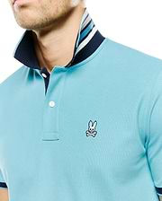 Men's Klaus Pique Polo, a light blue classic fit pique knit polo with a navy collar, two-button placket, and multi-striped inner collar, featuring the iconic embroidered Psycho Bunny skull logo on the left chest. (2)