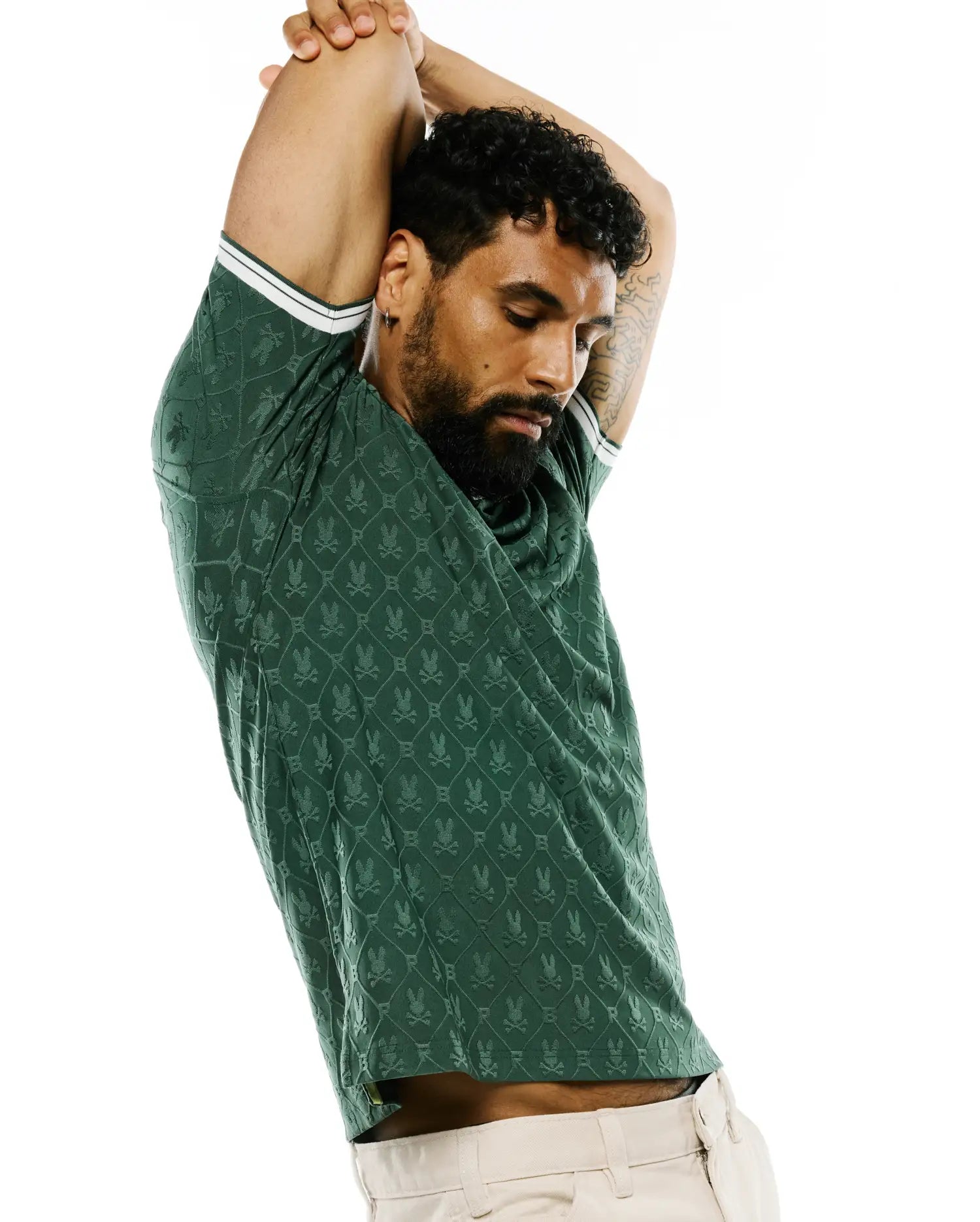 Mens Garry Jacquard Johnny Collar Polo in dark green, featuring an all-over jacquard Psycho Bunny skull logo pattern in a diamond grid, slim fit, and white double-stripe trim on sleeve cuffs. (4)
