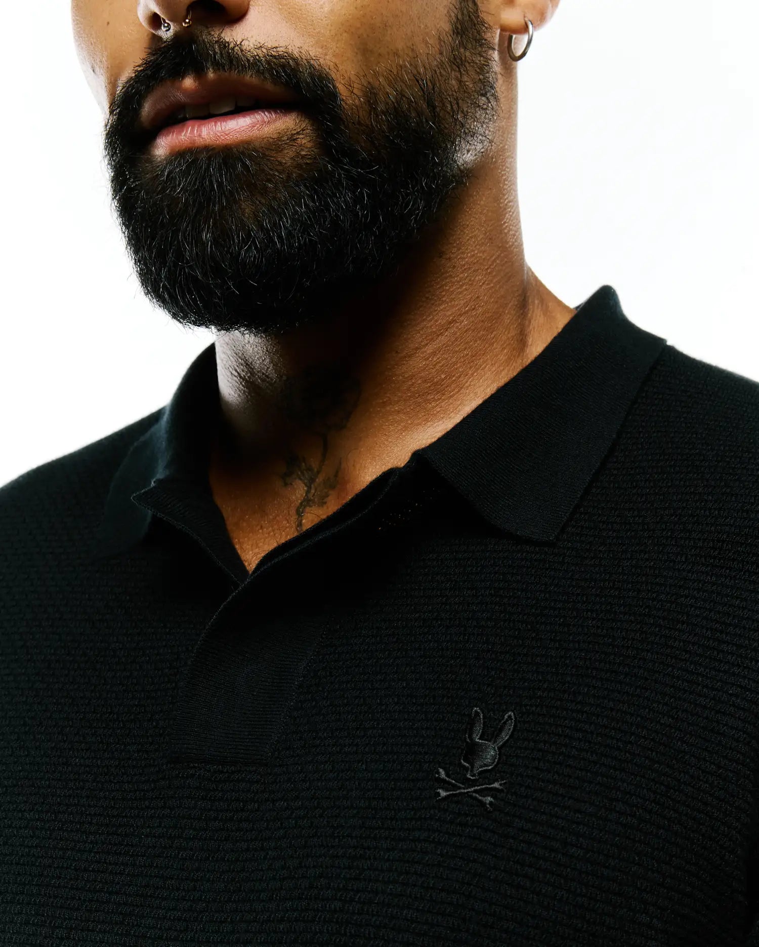 Black Mens Leroy Long Sleeve Knit Polo with a textured pique-like fabric, featuring a small, tonal embroidered Psycho Bunny skull logo on the left chest.