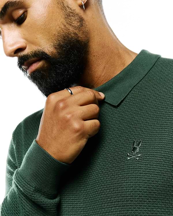 Mens Leroy Long Sleeve Knit Polo in deep forest green, featuring a textured knit fabric, ribbed collar and cuffs, and a small, tonal embroidered Psycho Bunny skull logo on the left chest.