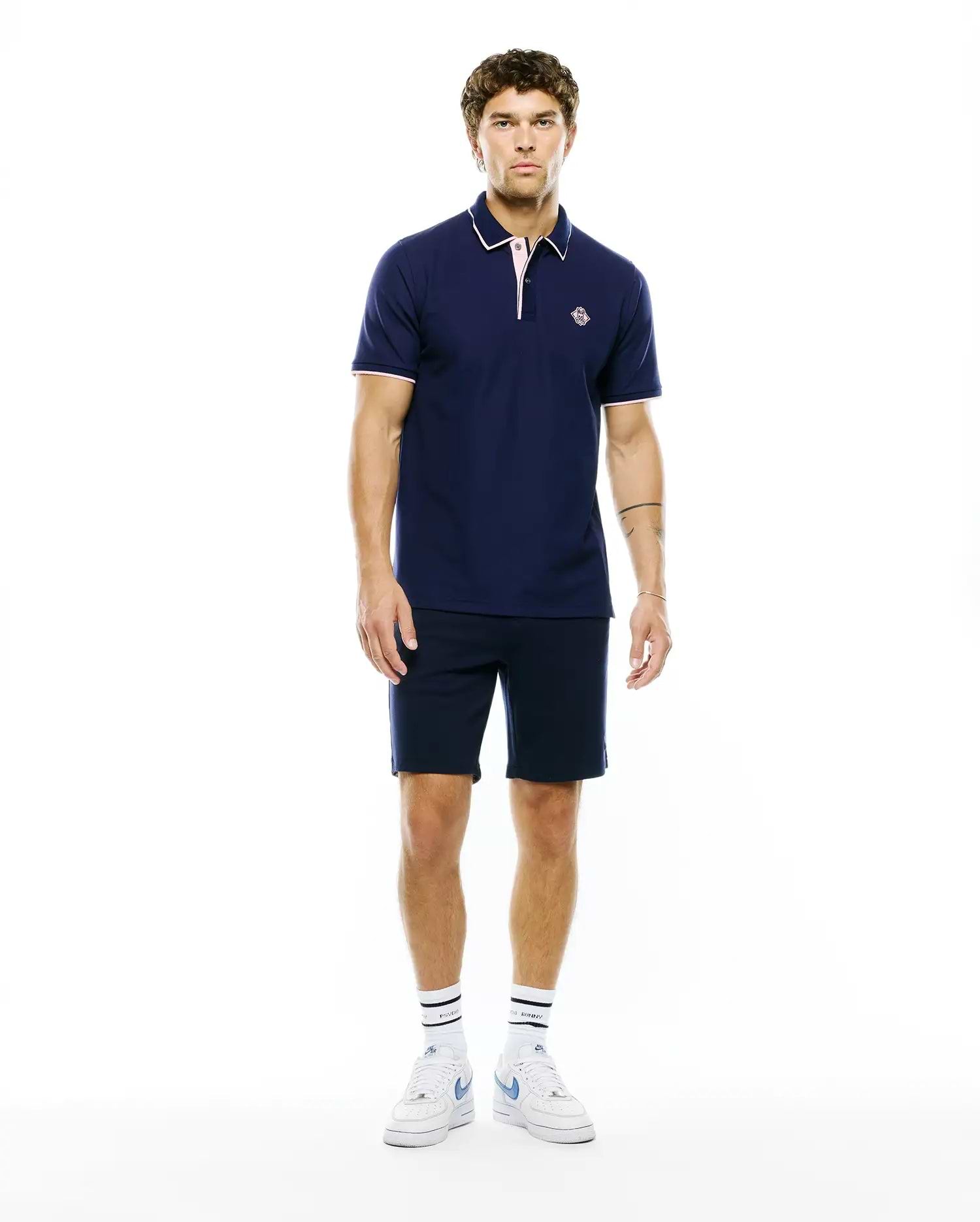MENS ROBIN PIQUE POLO in navy, classic fit, with white collar tipping, pink placket and cuff trim, and a small embroidered Psycho Bunny skull logo on the left chest.