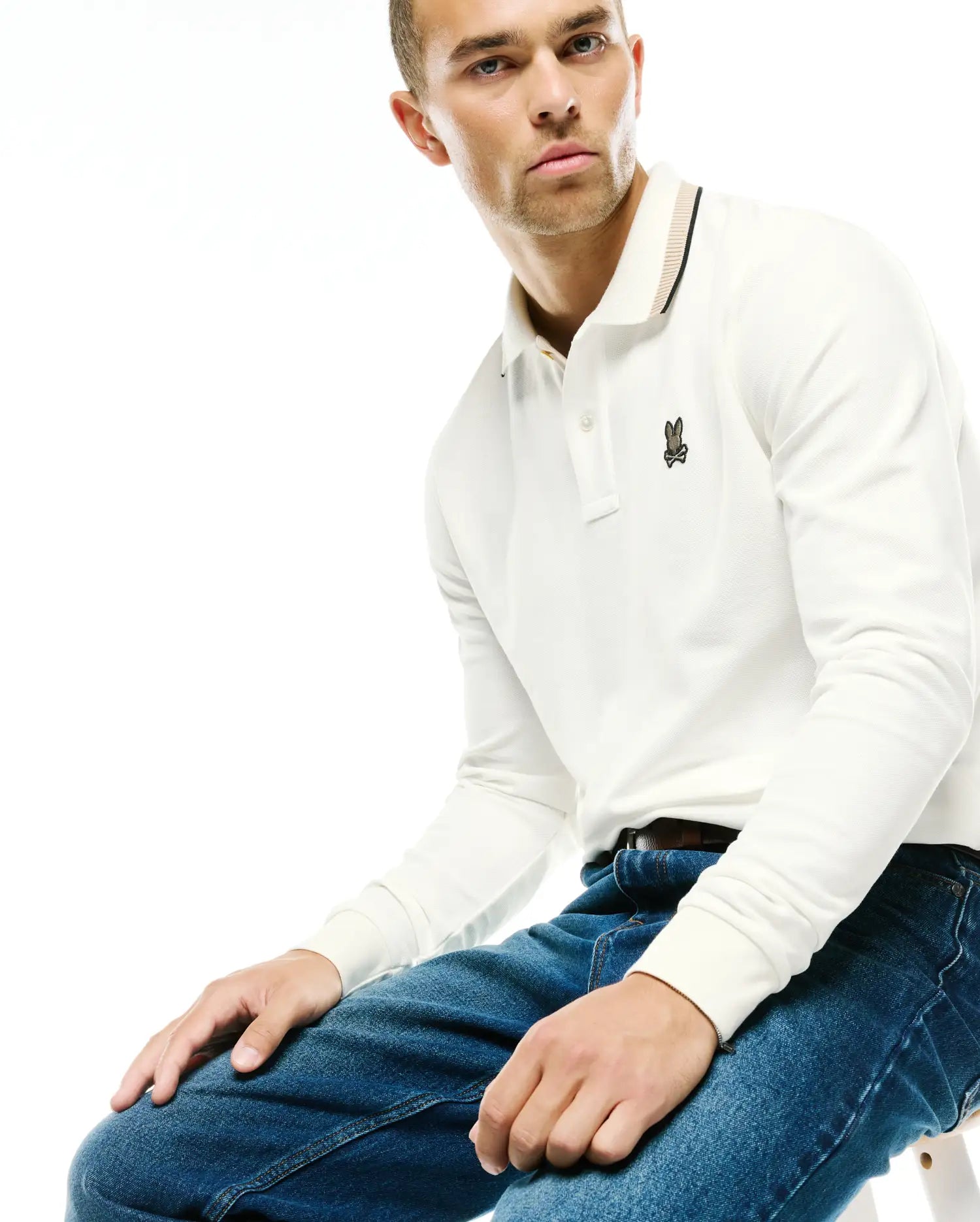 Men's Grover Pique Longsleeve Polo in white, featuring a classic fit, textured pique fabric, and a small embroidered Psycho Bunny skull logo on the left chest, with a striped collar in black and tan. (3)