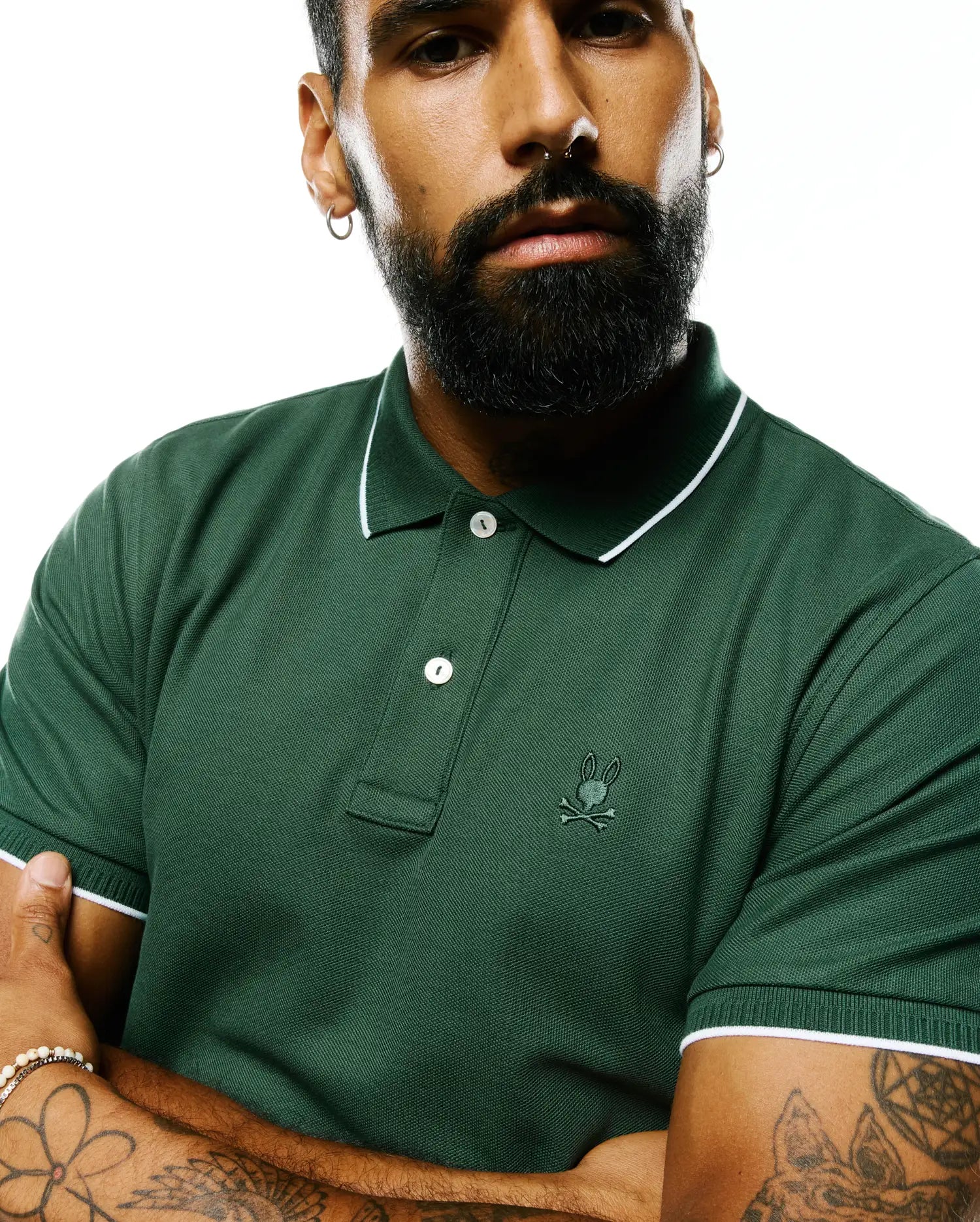 Mens Ringston Pique Polo in forest green pique knit, featuring a classic fit, white tipping on the ribbed collar and cuffs, two white buttons, and a small embroidered Psycho Bunny skull logo on the left chest.