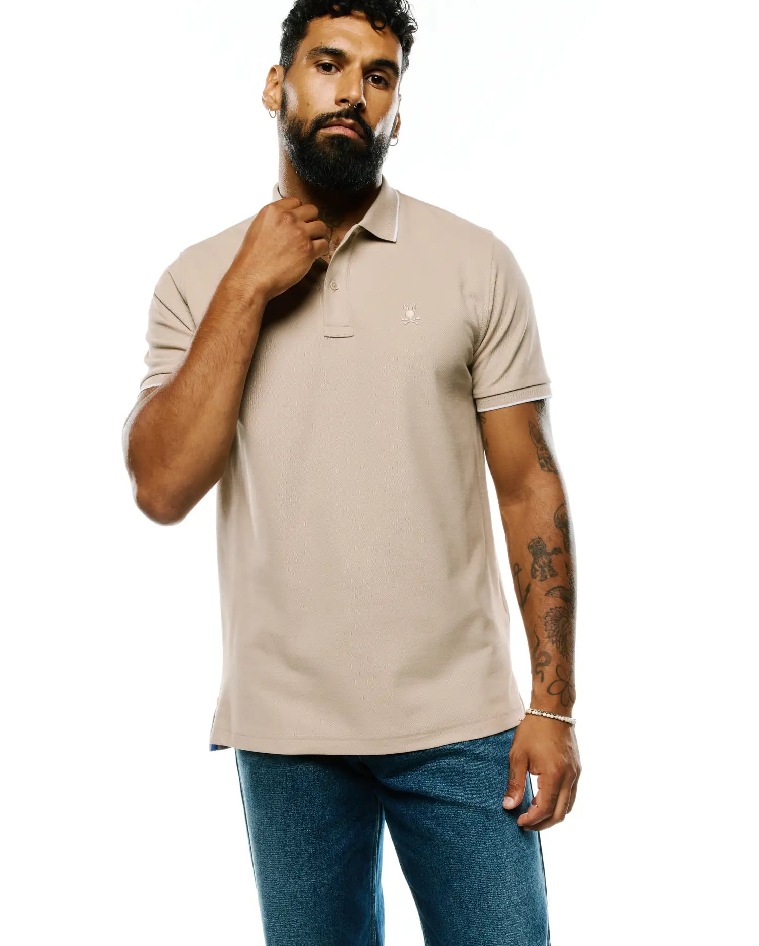 Mens Ringston Pique Polo in classic fit beige pique knit, featuring white tipping on the ribbed collar and cuffs, with a small embroidered Psycho Bunny skull logo on the left chest.