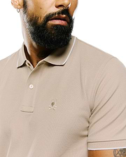 Mens Ringston Pique Polo in classic fit beige pique fabric, featuring a two-button placket, white tipping on the ribbed collar and cuffs, and a small embroidered Psycho Bunny skull logo on the left chest.