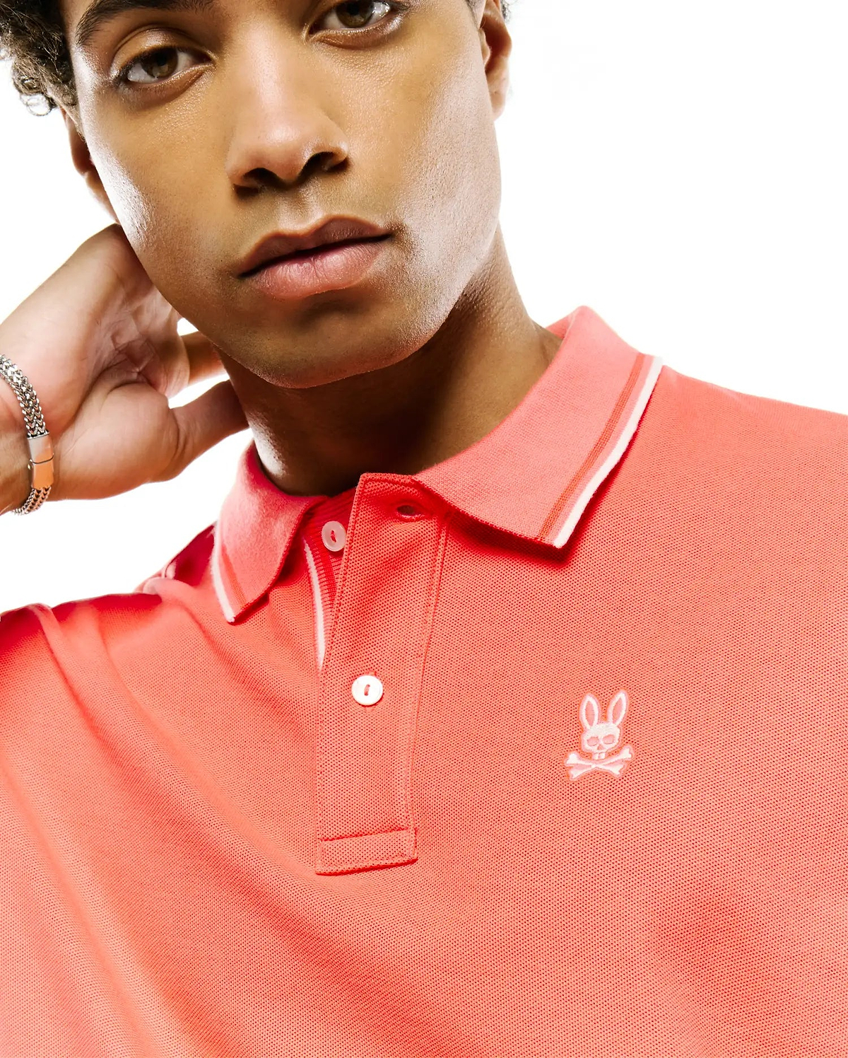 Mens Atley Pique Polo, vibrant coral, classic fit, pique knit. Features a two-button placket, ribbed collar with white tipping, and a small white embroidered Psycho Bunny skull logo on the left chest. (2)