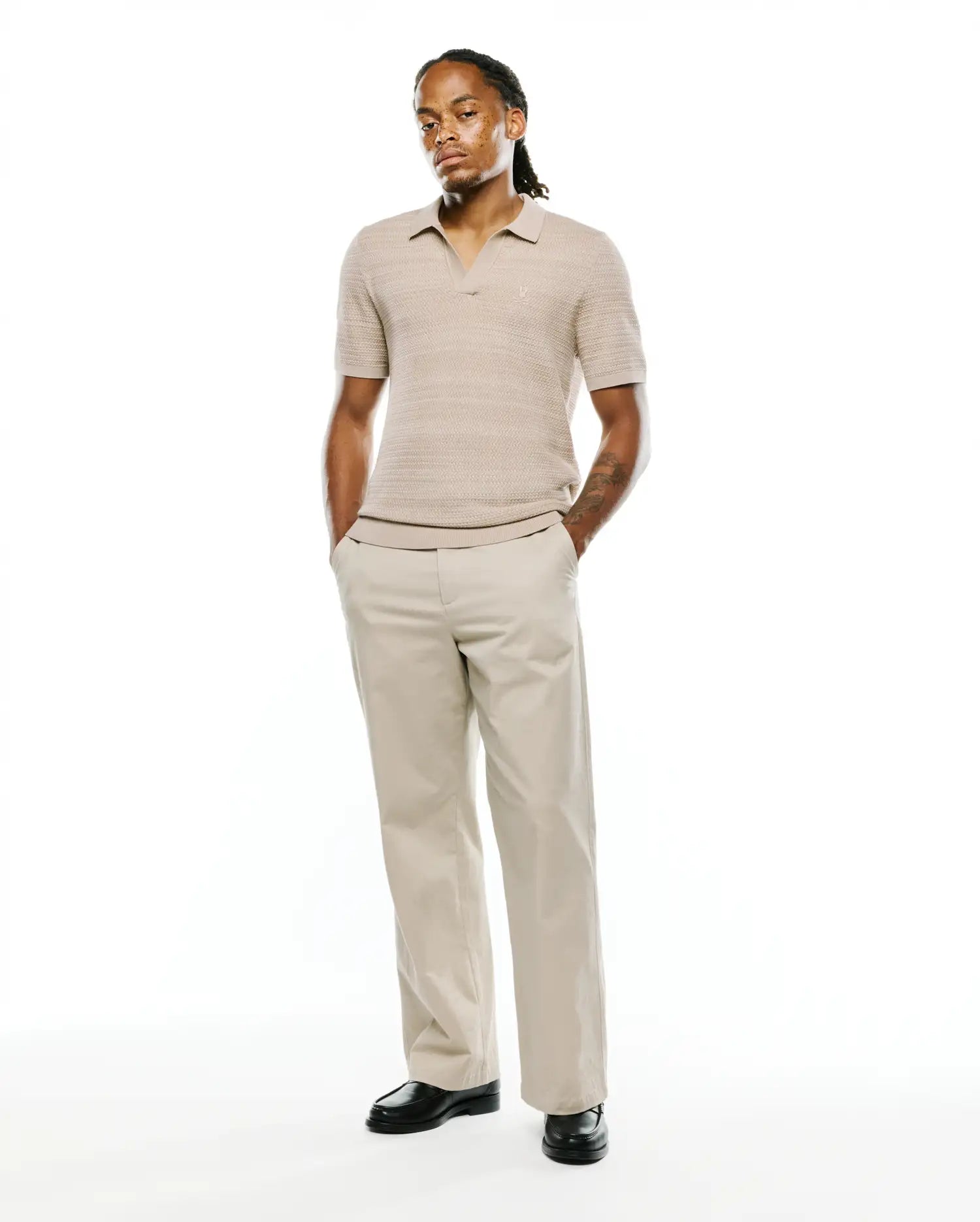 Mens Devon Braided Stitch Knit Polo in light tan, featuring a classic fit, intricate braided stitch knit texture, an open collar, and a small embroidered Psycho Bunny skull logo on the left chest.