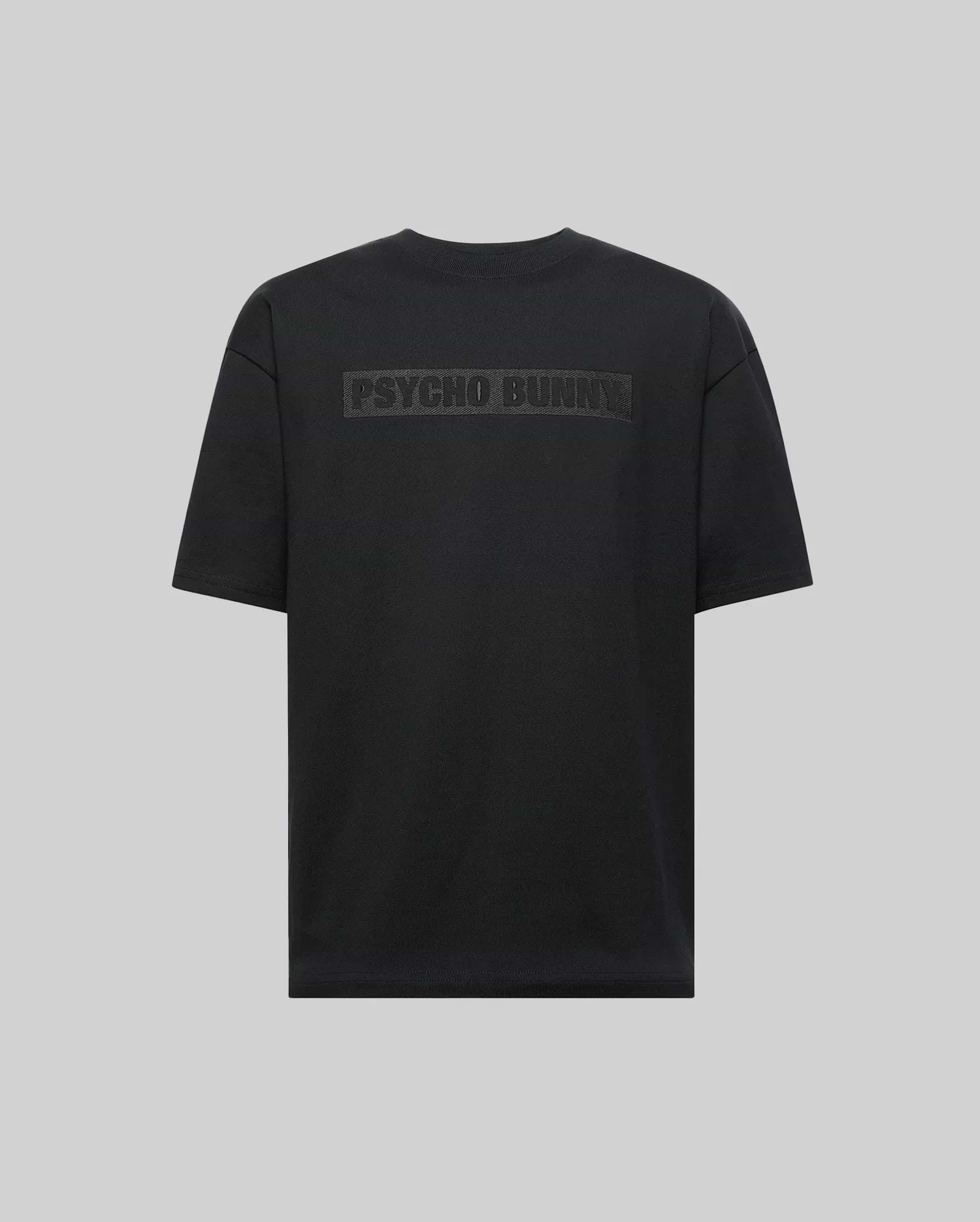 The Psycho Bunny MENS ZAYN OVERSIZED GRAPHIC TEE (MT0200004) is a black, heavyweight jersey short-sleeve shirt with bold "PSYCHO BUNNY" lettering on the upper back, shown on a light gray background.