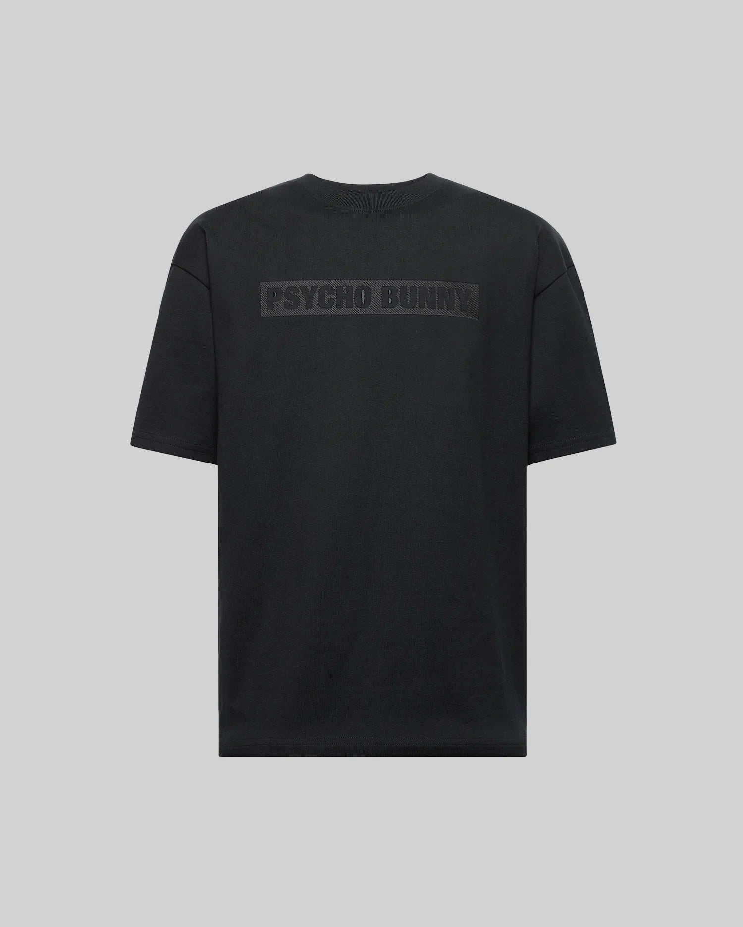 The Psycho Bunny MENS ZAYN OVERSIZED GRAPHIC TEE (MT0200004) is a black, heavyweight jersey short-sleeve shirt with bold "PSYCHO BUNNY" lettering on the upper back, shown on a light gray background.