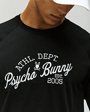 A man wears the Psycho Bunny MENS MATTEO RAGLAN GRAPHIC TEE (MT0200008), a black shirt with "ATHL DEPT Psycho Bunny EST. 2005" and a bunny logo, partially visible under a white cap. (3)