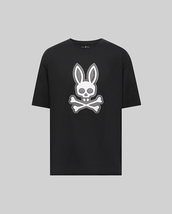 The Psycho Bunny MENS RYDER OVERSIZED FIT TEE (MT0200062) is a black Pima cotton shirt featuring a bold white bunny head with long ears over a skull and crossbones, all set on a plain gray background.