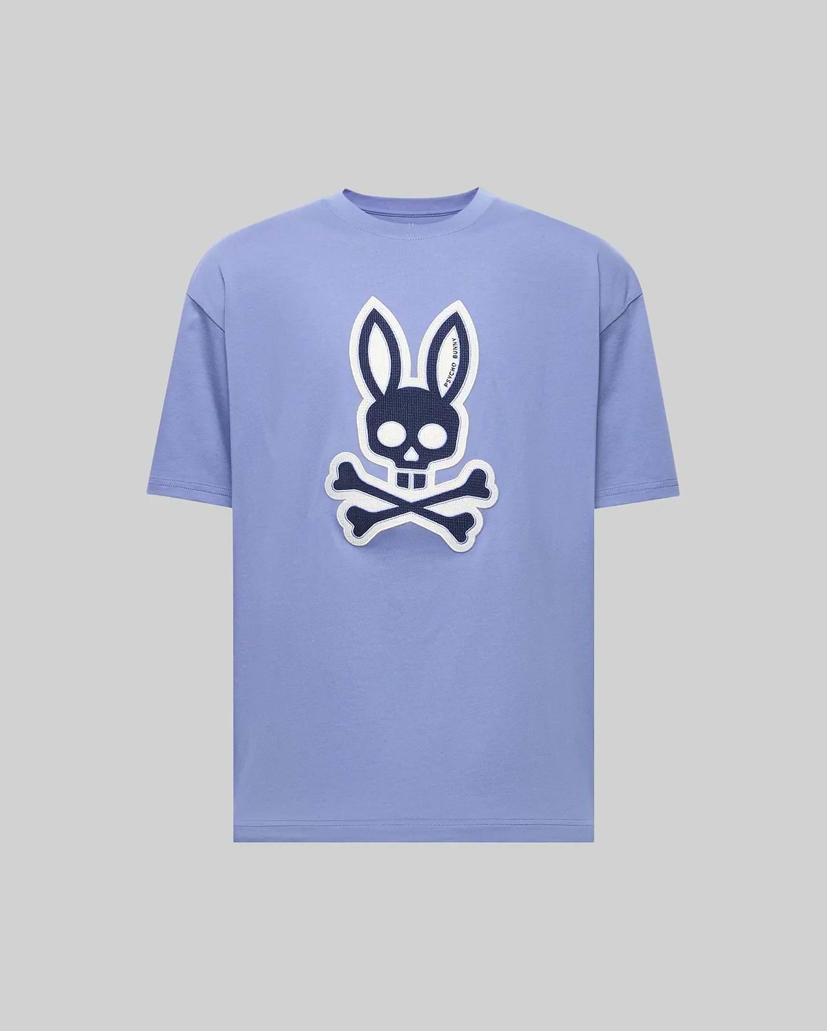 The Psycho Bunny MENS RYDER OVERSIZED FIT TEE (MT0200062) is a light purple premium tee with a bold black and white bunny skull and crossbones graphic on the front, shown against a plain gray background. (1)