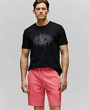 A man stands against a plain background, wearing the Psycho Bunny MENS OLLIE GRAPHIC TEE (MT0200066) in soft Pima cotton with a Bunny graphic and bright pink drawstring shorts, looking directly at the camera with a neutral expression. (2)