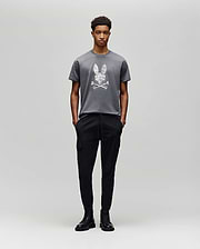 A person poses against a light gray background in the Psycho Bunny MENS GRANT BUNNY GRAPHIC TEE - MT0200081, crafted in Peru from soft Pima cotton, paired with black cargo pants and black lace-up boots. (5)