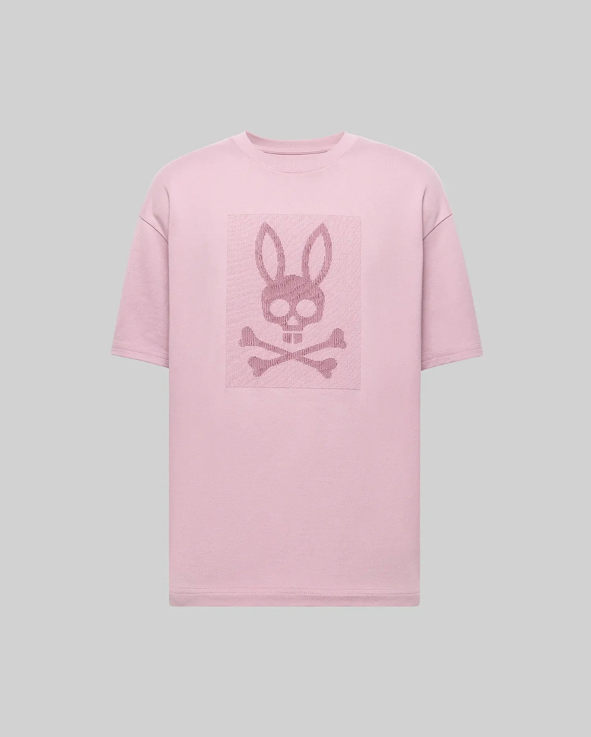 The Psycho Bunny MENS REECE OVERSIZED TEE (MT0200082) is a light pink, heavyweight jersey tee in a relaxed fit, featuring a centered skull with bunny ears above crossed bones on the chest against a plain gray background. (5)