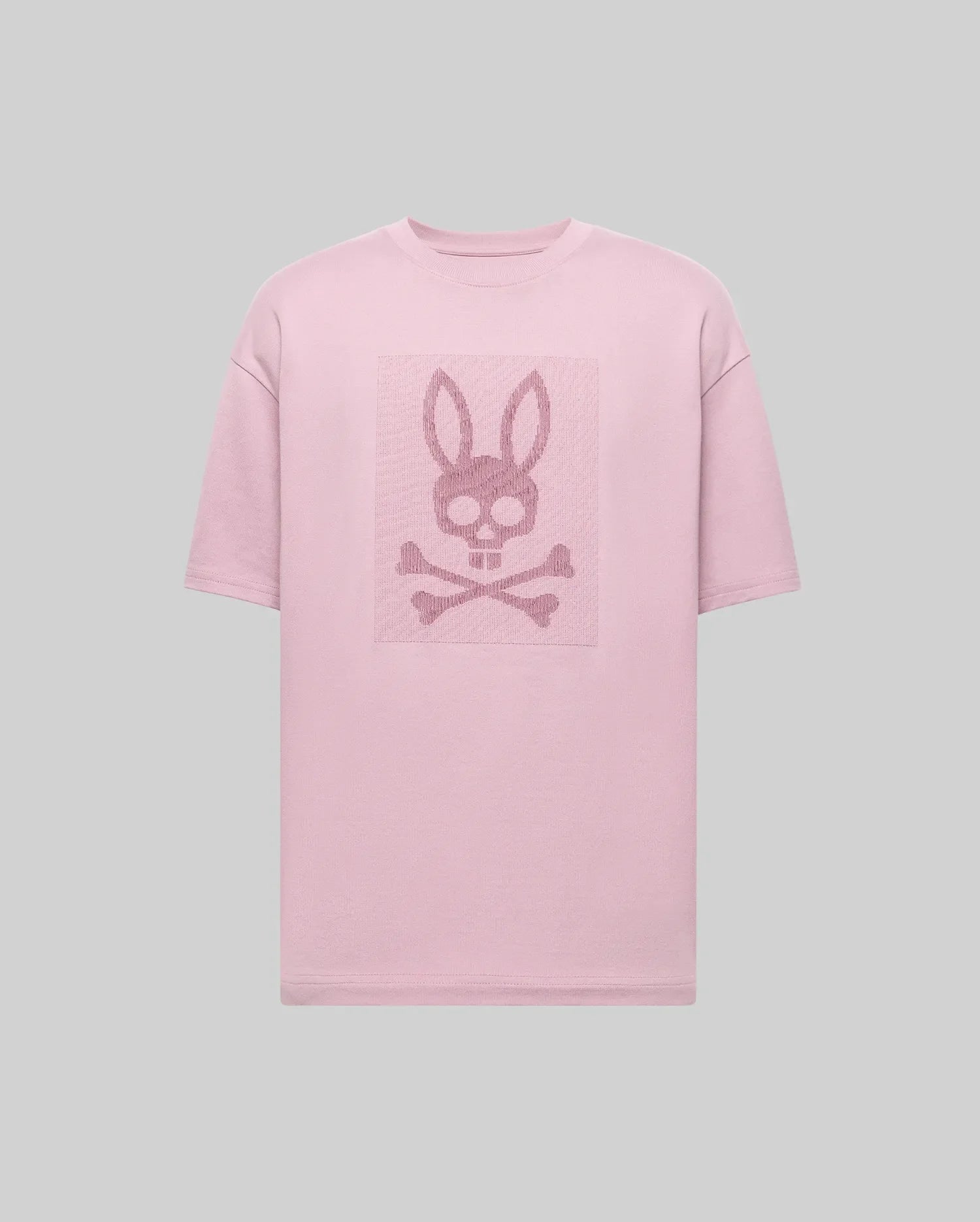 The Psycho Bunny MENS REECE OVERSIZED TEE (MT0200082) is a light pink, heavyweight jersey tee in a relaxed fit, featuring a centered skull with bunny ears above crossed bones on the chest against a plain gray background. (5)