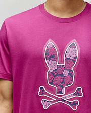 A person wearing the Psycho Bunny MENS ROWEN BUNNY GRAPHIC TEE (MT0200101), featuring a large bunny head and crossbones with a pink and purple floral pattern. Only the upper torso is visible. (3)