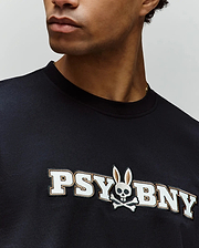 Wearing Psycho Bunny’s MENS WADE GRAPHIC TEE (MT0200105), a black 100% cotton regular fit shirt with “PSYBNY” text and a skull with bunny ears and crossbones logo; only the lower face and upper torso are visible. (3)