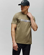 A man in a black cap and the Psycho Bunny MENS WADE GRAPHIC TEE (MT0200105)—olive-green with "PSYBUNY" and a cartoon bunny graphic—stands against a light gray background, looking sideways with one hand on his neck. (4)