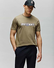 A man in a regular fit, 100% cotton olive green MENS WADE GRAPHIC TEE - MT0200105 by Psycho Bunny with a "PSYBNY" and cartoon bunny logo stands with one hand in his pocket, wearing a black cap against a light gray background. (2)