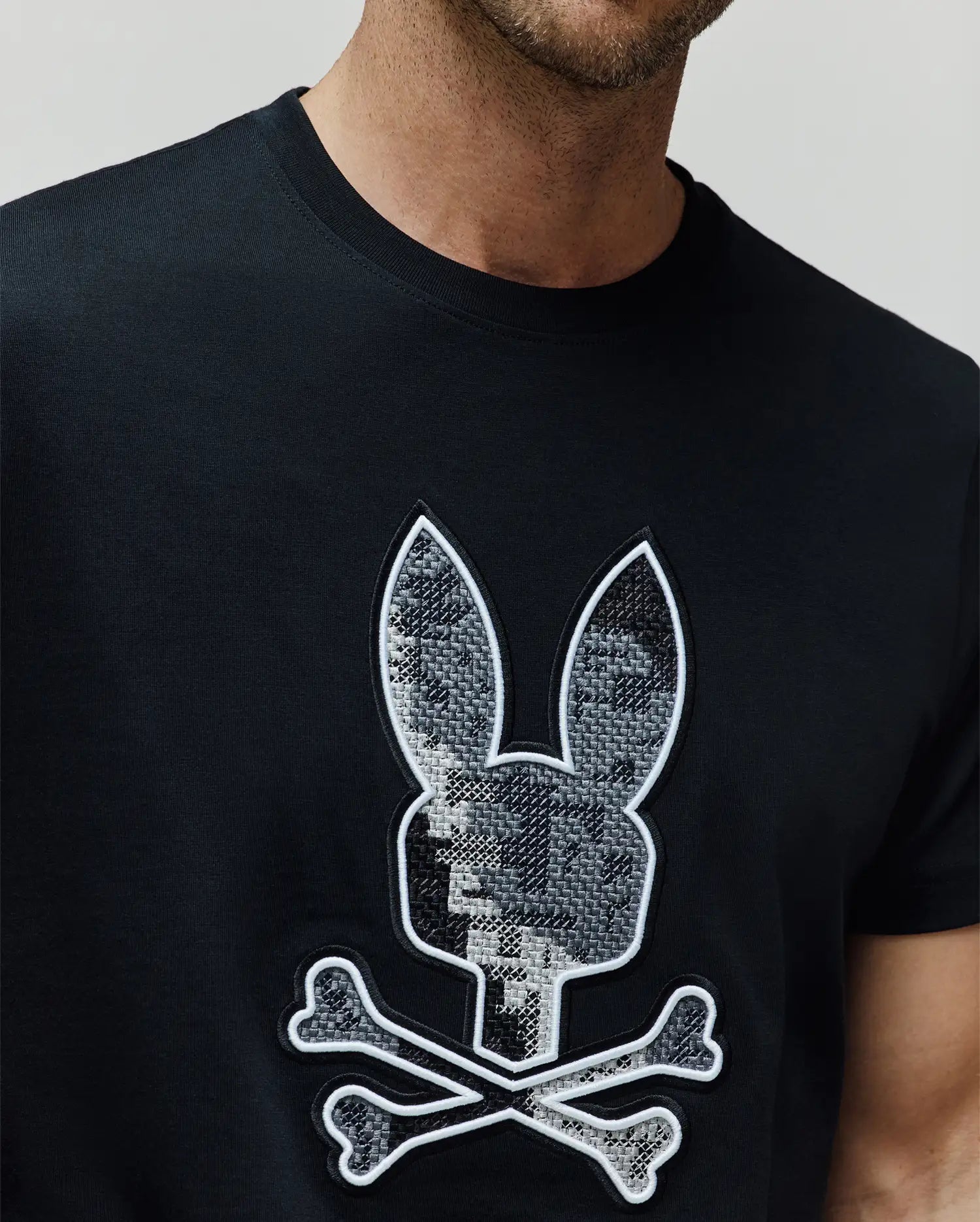 Mens Olivier Graphic Tee, black classic-fit jersey t-shirt with a large, central chest embroidered Psycho Bunny skull and crossbones logo featuring a grey and white textured fill and white outline. (3)