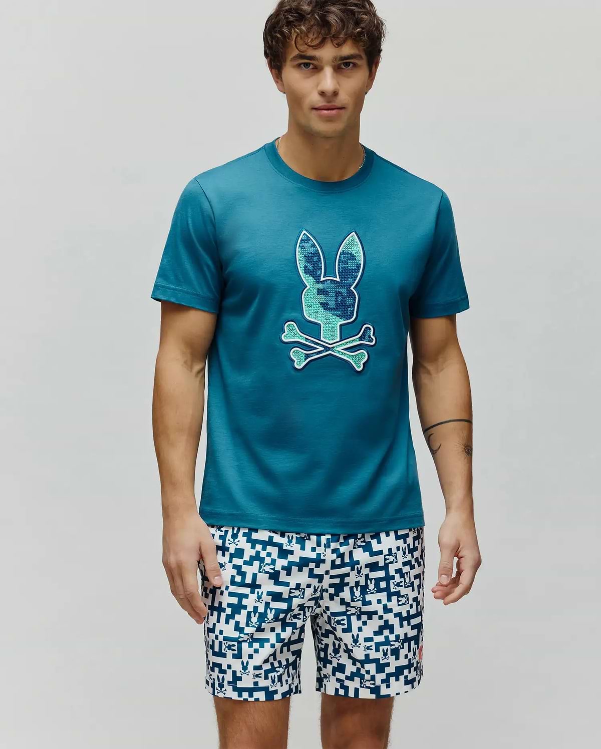 Mens Olivier Graphic Tee, a classic fit teal jersey t-shirt with a large, textured blue and green pixelated Psycho Bunny skull logo centered on the chest. (4)