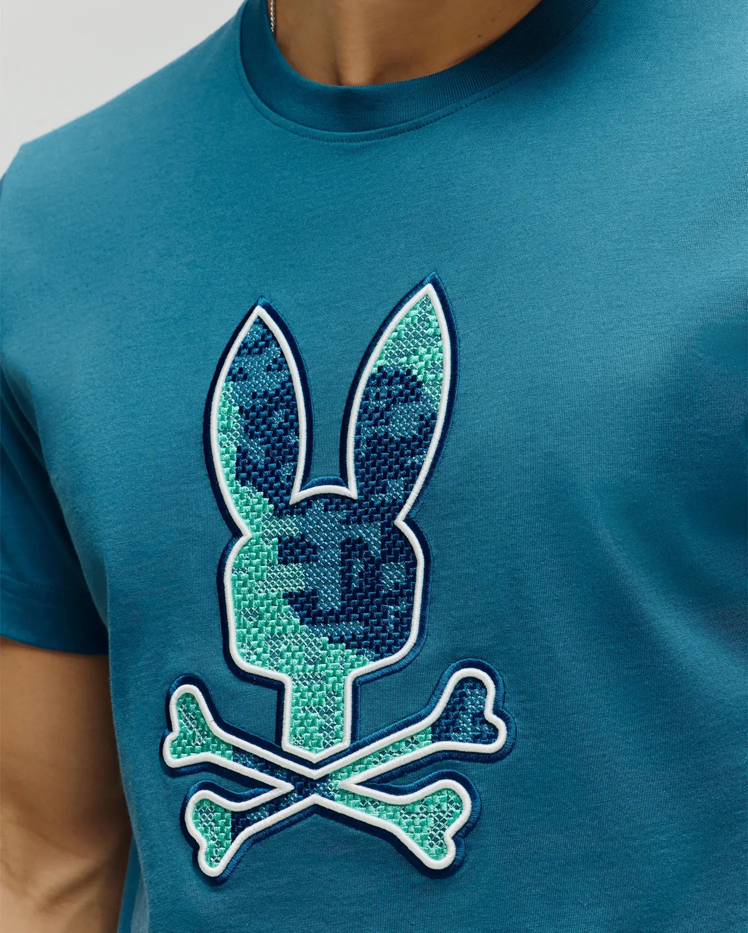 Mens Olivier Graphic Tee in teal, featuring a large central embroidered pixelated green and dark blue bunny skull logo with white outline on soft jersey knit fabric, classic fit. (3)