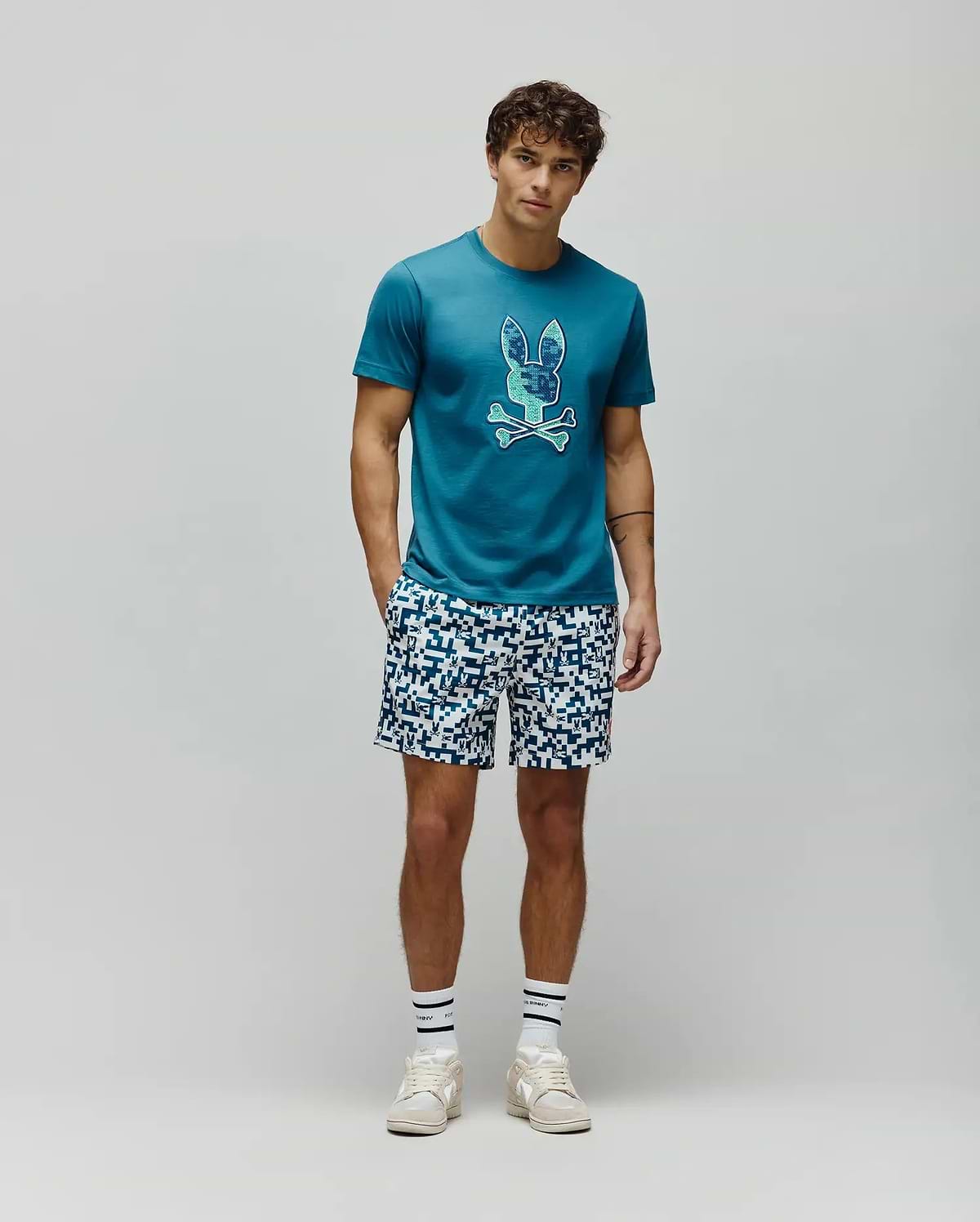 Mens Olivier Graphic Tee in teal jersey knit, featuring a classic fit and a large, pixelated blue and green Psycho Bunny skull logo prominently displayed on the chest. (5)