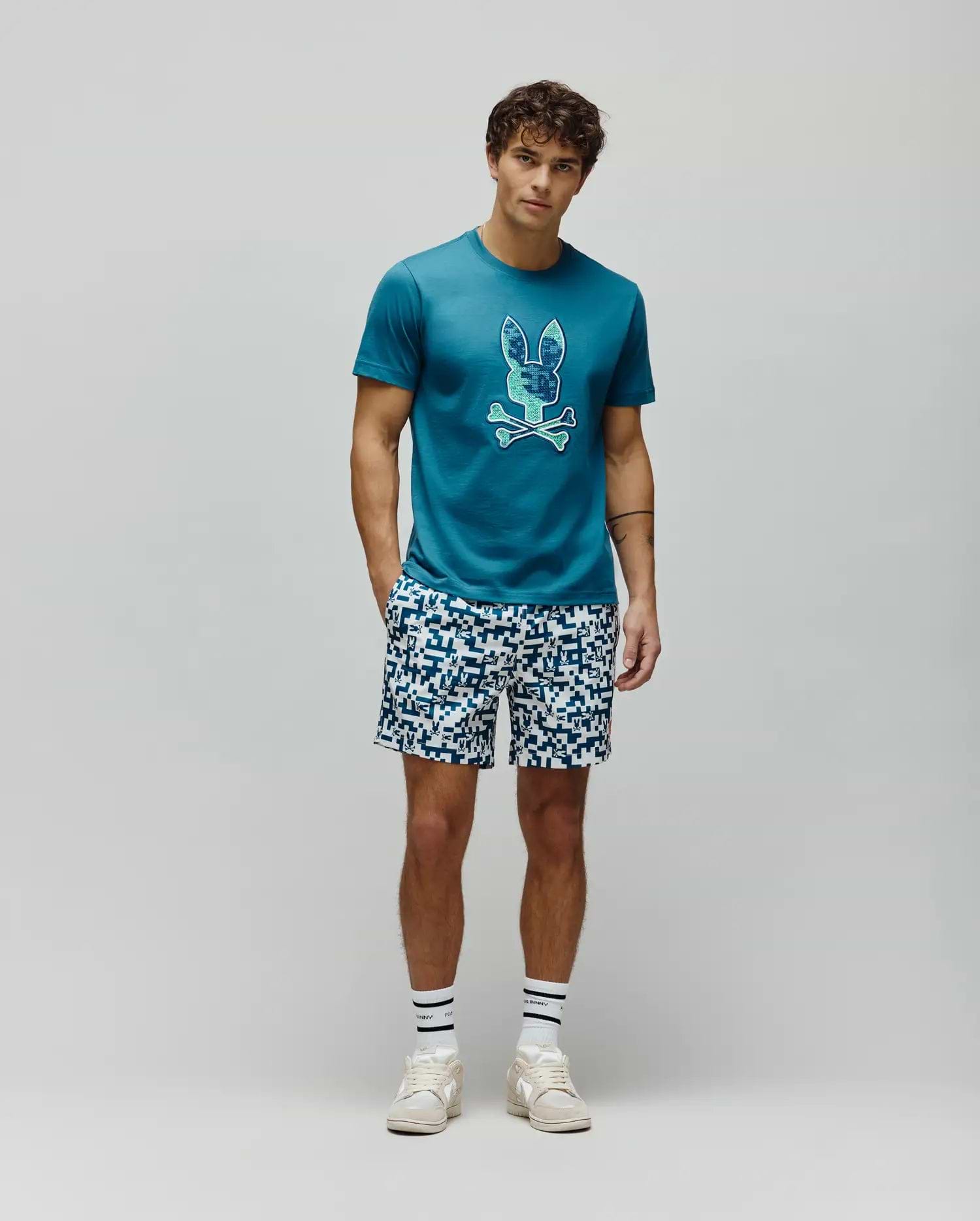 Mens Olivier Graphic Tee in teal jersey knit, featuring a classic fit and a large, pixelated blue and green Psycho Bunny skull logo prominently displayed on the chest. (5)