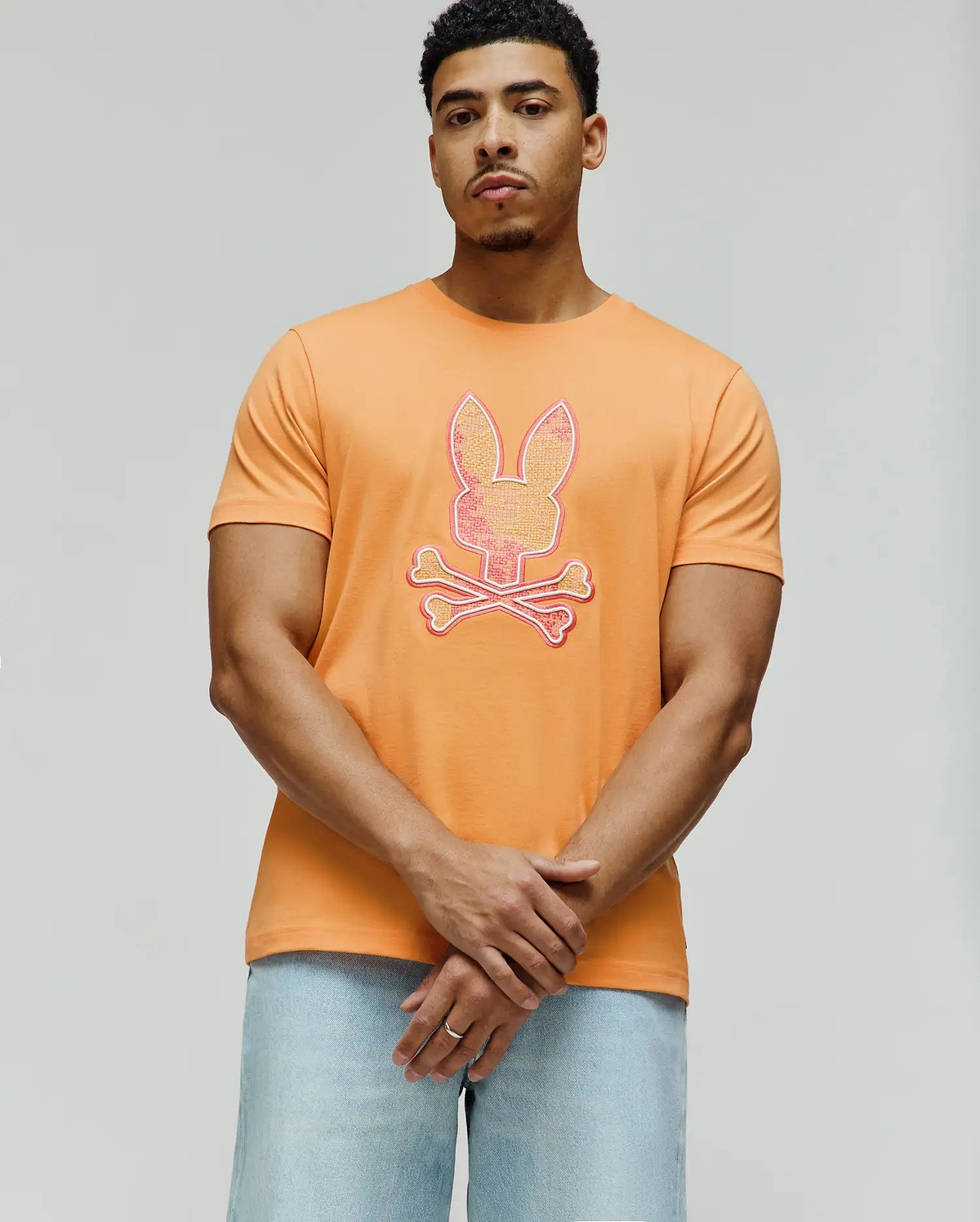 Vibrant Orange Mens Olivier Graphic Tee, classic fit, smooth jersey knit, featuring a large, textured pink, yellow, and white Psycho Bunny skull and crossbones graphic on the chest. (4)