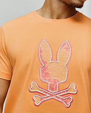 Mens Olivier Graphic Tee in peach jersey knit, featuring a large, central embroidered Psycho Bunny skull logo with pink and orange cross-stitch texture and white outline. (3)