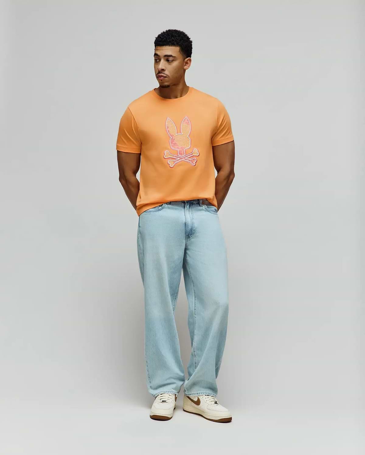 Mens Olivier Graphic Tee, a classic fit orange jersey t-shirt featuring a large, vibrant pink and white outlined Psycho Bunny skull graphic prominently centered on the chest. (5)