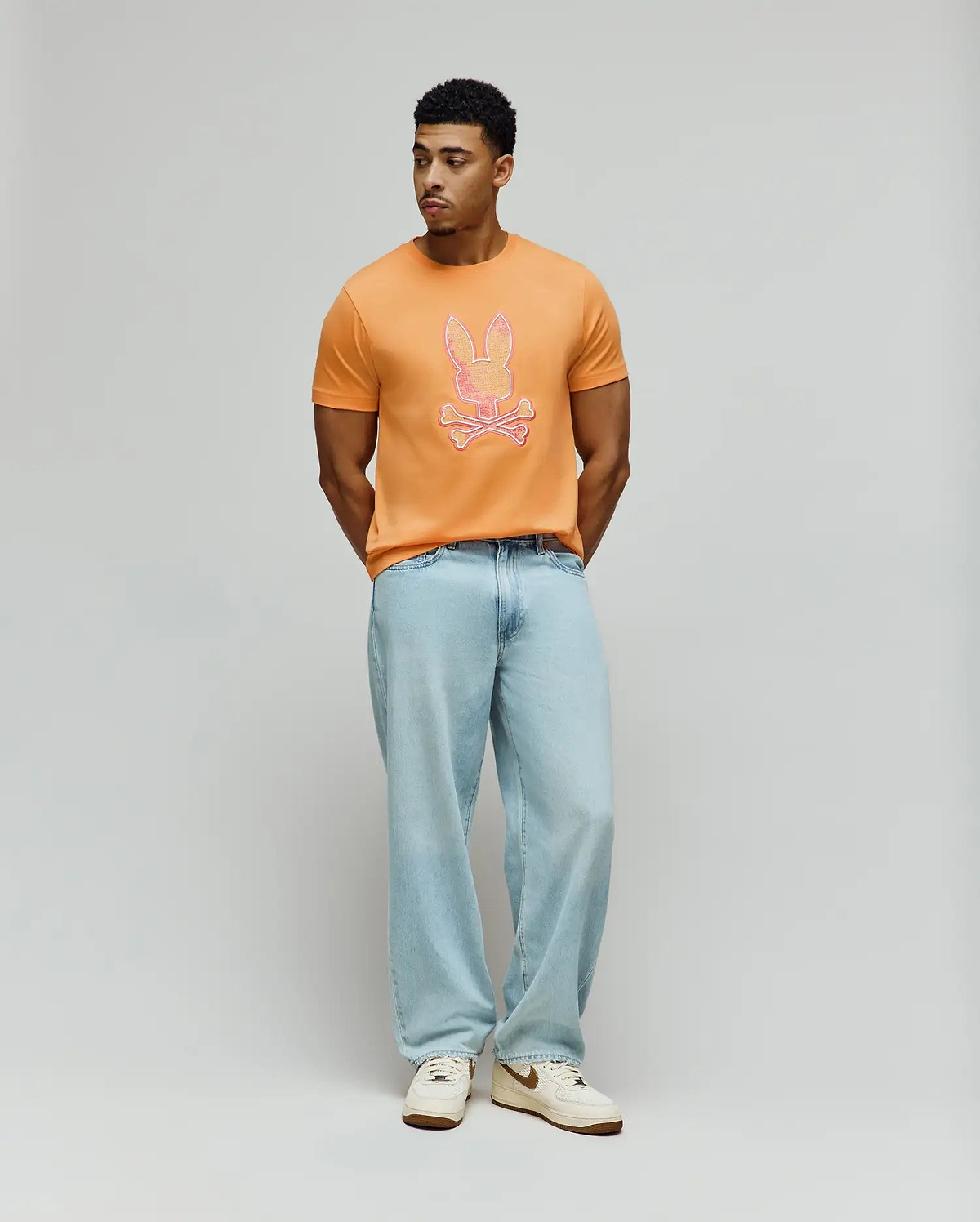 Mens Olivier Graphic Tee, a classic fit orange jersey t-shirt featuring a large, vibrant pink and white outlined Psycho Bunny skull graphic prominently centered on the chest. (5)