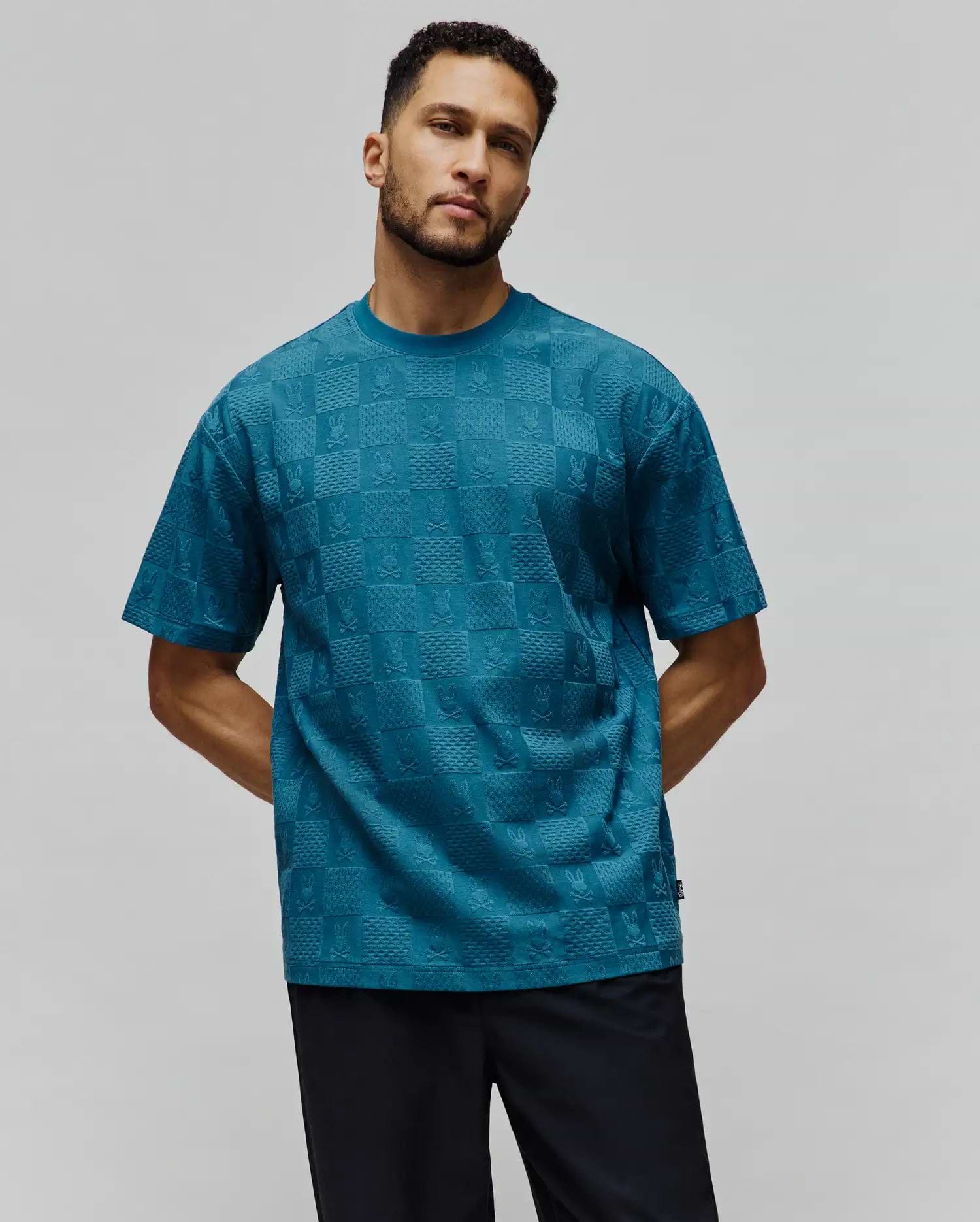 Mens Dustin Oversized Tee in teal, featuring an all-over embossed checkerboard pattern with alternating Psycho Bunny skull logos and textured squares, finished with a small brand tag. (4)
