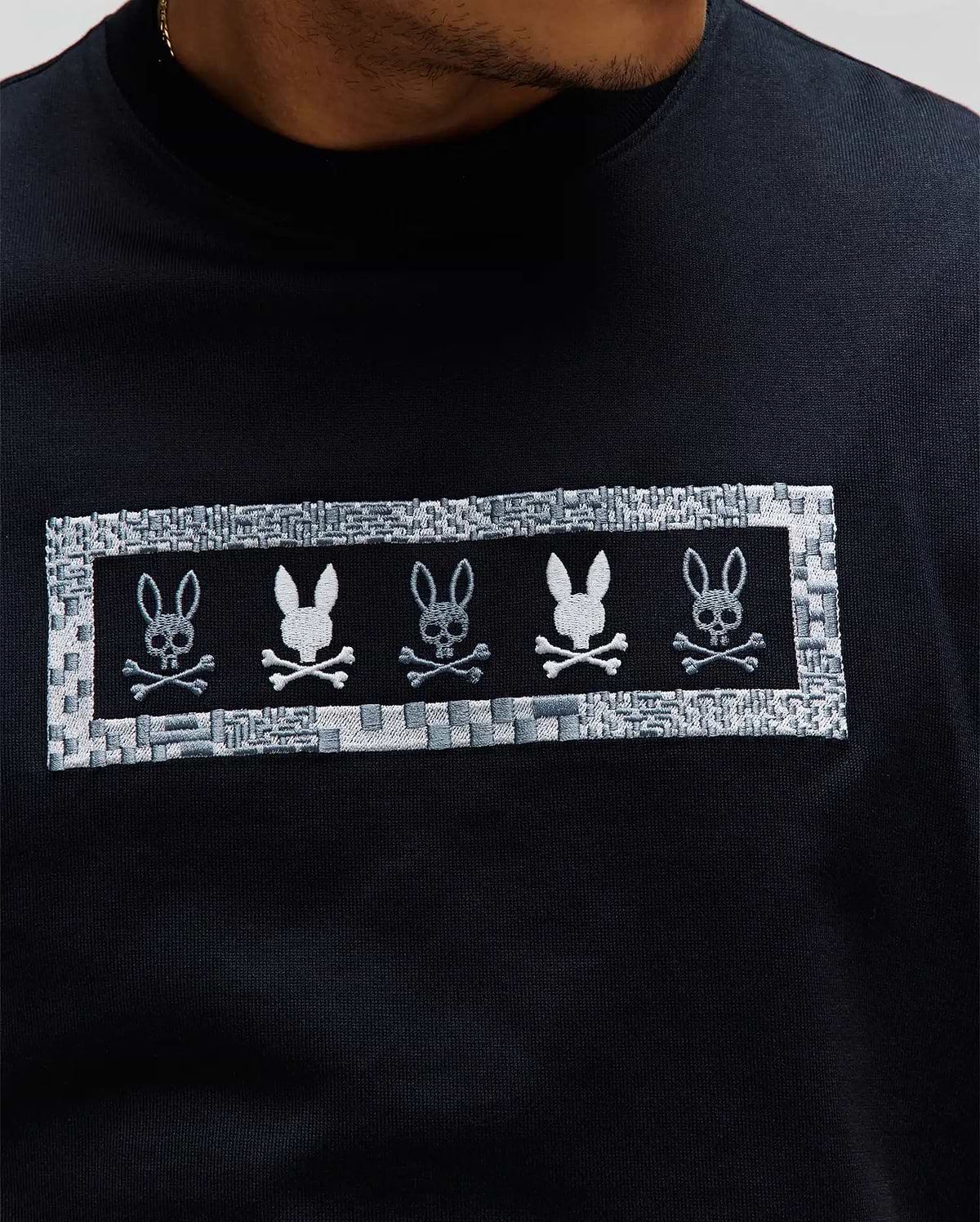 Mens Olivier Oversized Tee, black jersey knit, oversized fit, featuring a prominent chest embroidery of five Psycho Bunny skull logos in white and grey within a textured patterned border. (2)
