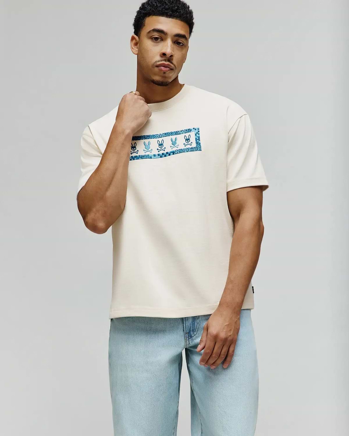 Mens Olivier Oversized Tee in cream jersey knit, featuring a large central chest graphic with repeating blue Psycho Bunny skull logos and a checkerboard pattern. (1)