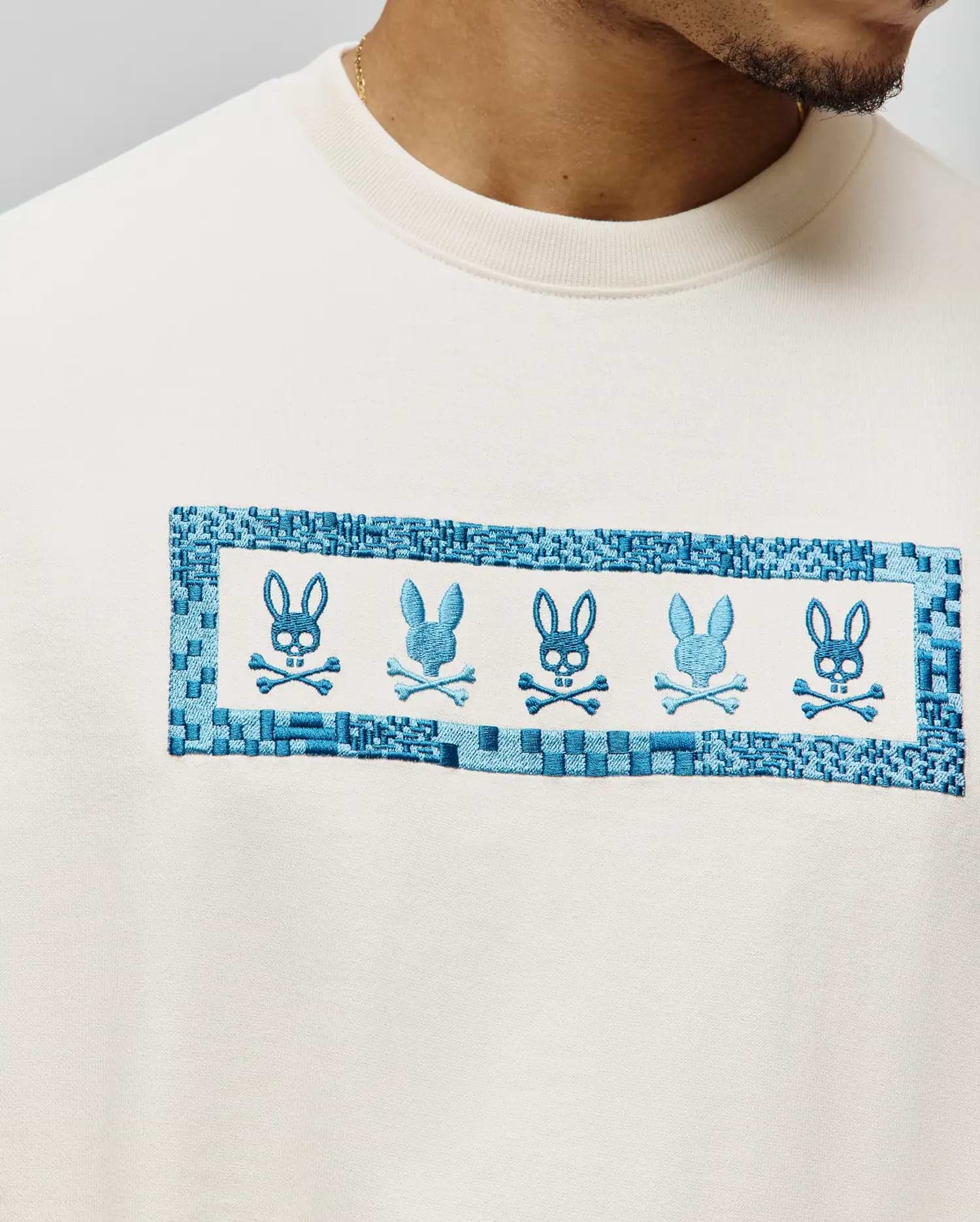Mens Olivier Oversized Tee in cream, featuring a large central chest embroidery with five alternating blue Psycho Bunny skull logos framed by a woven-look blue border on soft jersey fabric. (2)