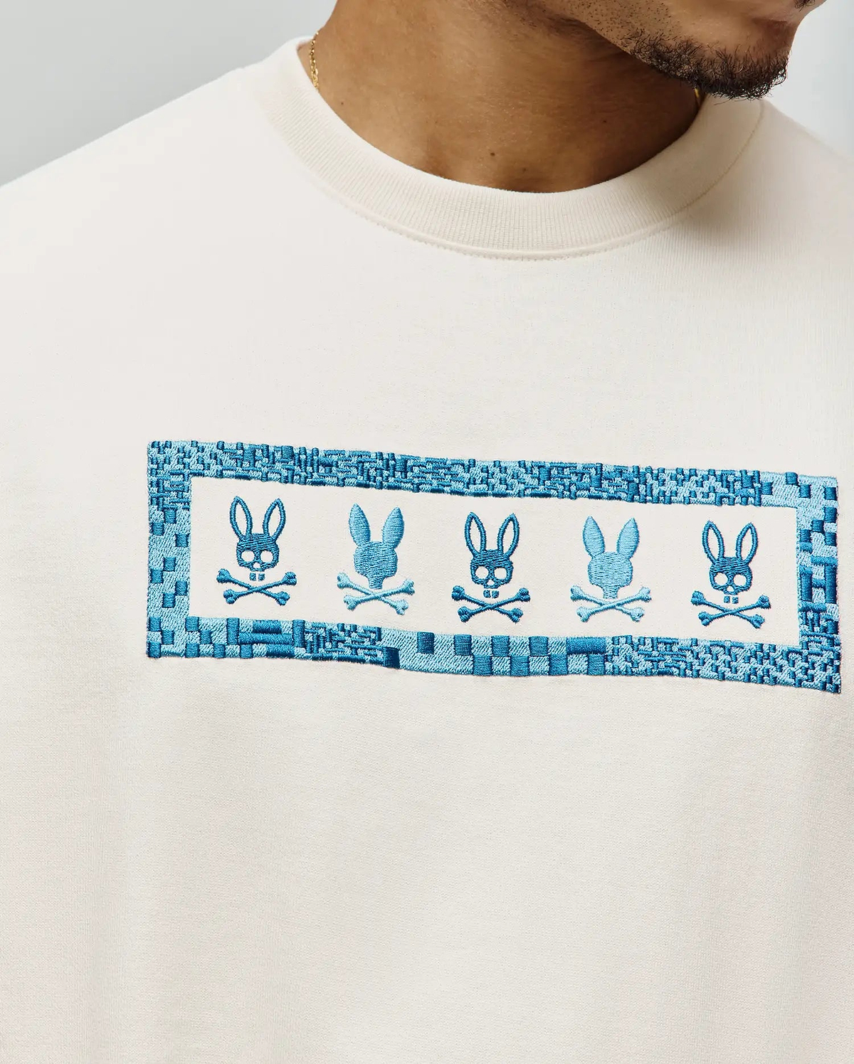 Mens Olivier Oversized Tee in cream, featuring a large central chest embroidery with five alternating blue Psycho Bunny skull logos framed by a woven-look blue border on soft jersey fabric. (2)