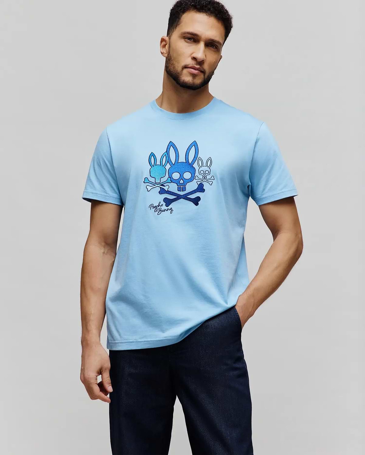 Mens Oscar Graphic Tee, light blue classic fit jersey knit t-shirt with a large central chest graphic featuring multiple blue Psycho Bunny skull logos, crossbones, and script. (5)