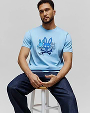 Mens Oscar Graphic Tee, a sky blue classic fit jersey t-shirt featuring a prominent chest graphic of three blue Psycho Bunny skull logos with crossbones and signature script. (3)
