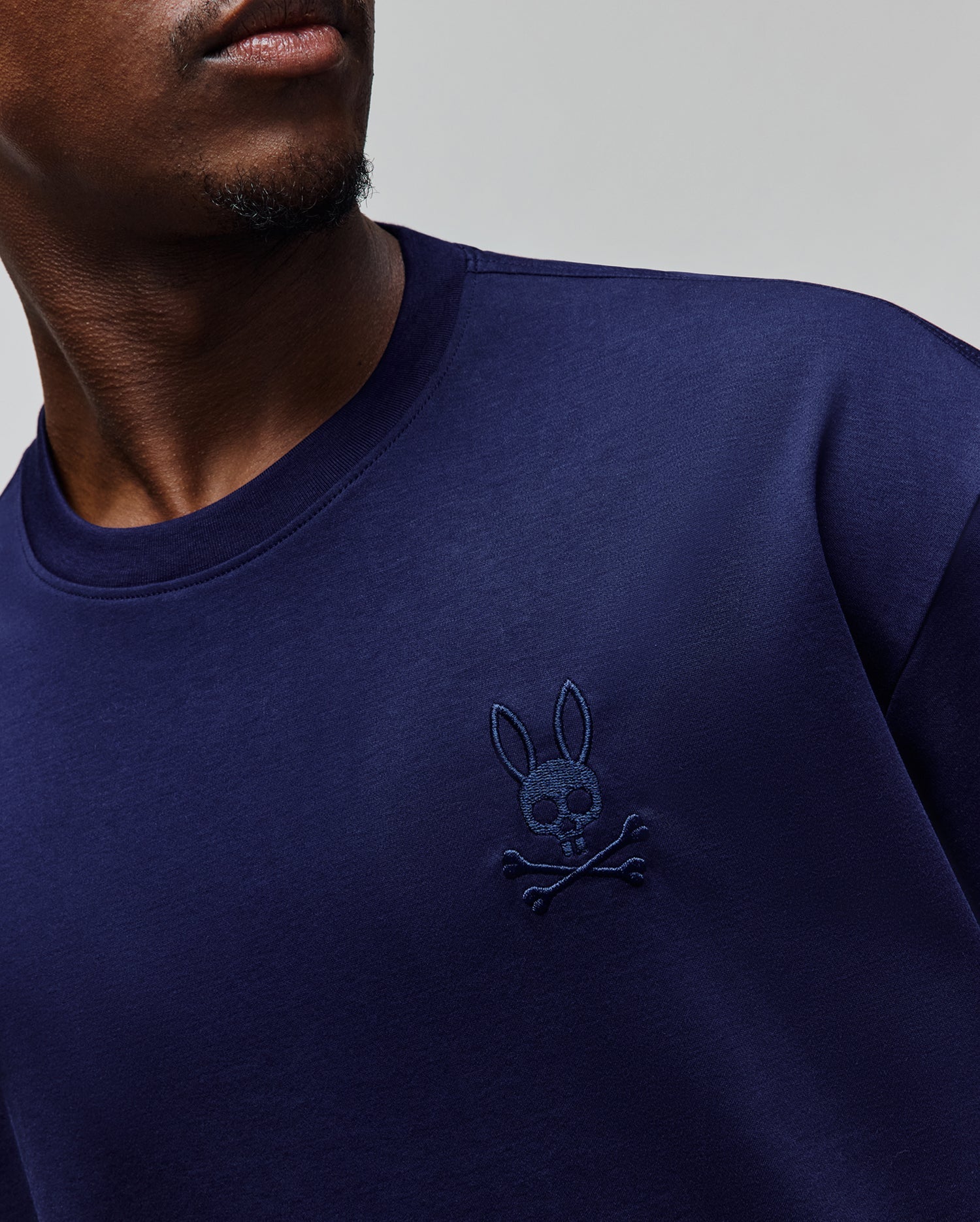 Mens Oscar Oversized Tee in navy blue, featuring a small, tonal embroidered Psycho Bunny skull and crossbones logo on the left chest, crafted from smooth jersey knit fabric.