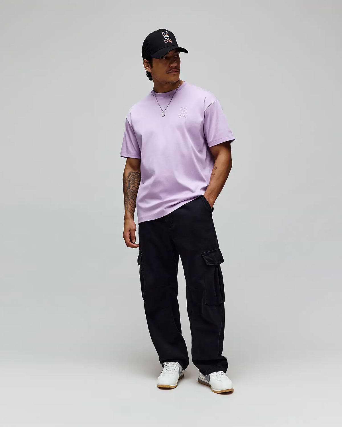 Lavender jersey Mens Oscar Oversized Tee with a white embroidered Psycho Bunny logo on the left chest, black relaxed cargo pants, and a black cap featuring the iconic white-red bunny skull. (3)