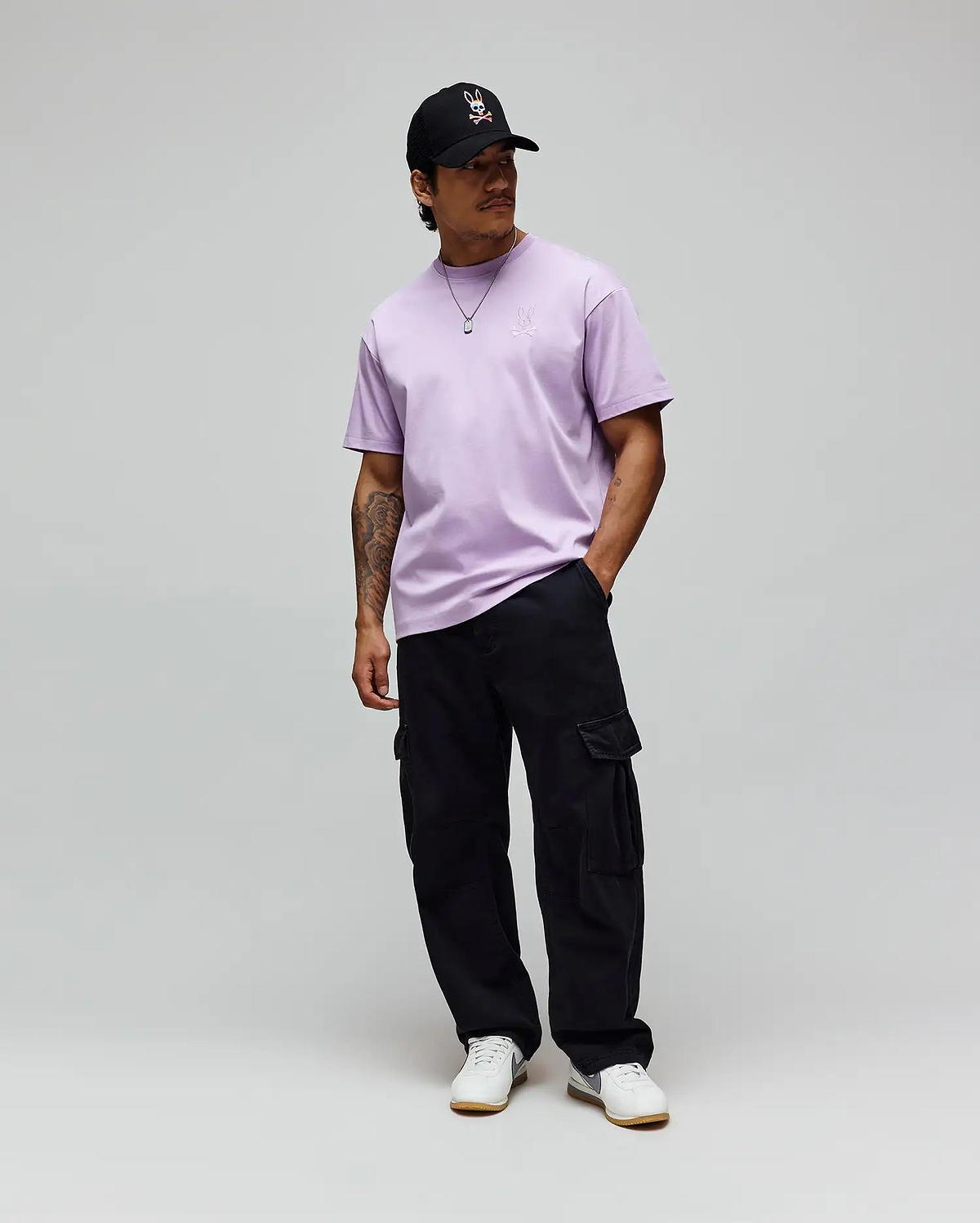 Lavender jersey Mens Oscar Oversized Tee with a white embroidered Psycho Bunny logo on the left chest, black relaxed cargo pants, and a black cap featuring the iconic white-red bunny skull. (3)