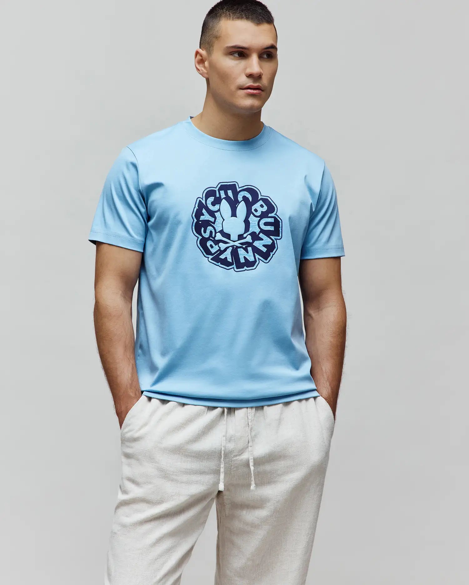 Mens Toby Graphic Tee, sky blue classic fit jersey t-shirt with a large central navy blue circular graphic featuring the iconic Psycho Bunny skull and text.