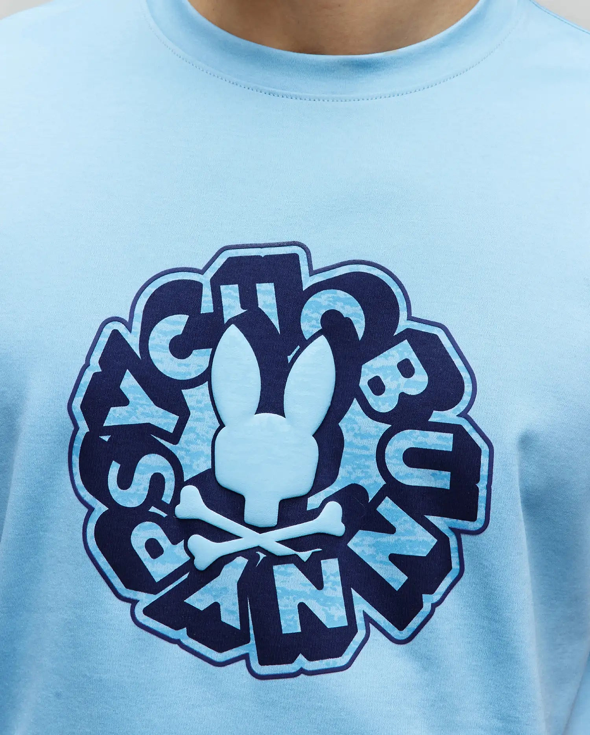 Mens Toby Graphic Tee, light blue jersey knit t-shirt with a large central chest graphic featuring a raised light blue Psycho Bunny skull and crossbones, surrounded by distressed dark blue and light blue stylized Psycho Bunny text.