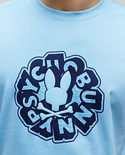 Mens Toby Graphic Tee, light blue jersey knit t-shirt with a large central chest graphic featuring a raised light blue Psycho Bunny skull and crossbones, surrounded by distressed dark blue and light blue stylized Psycho Bunny text.