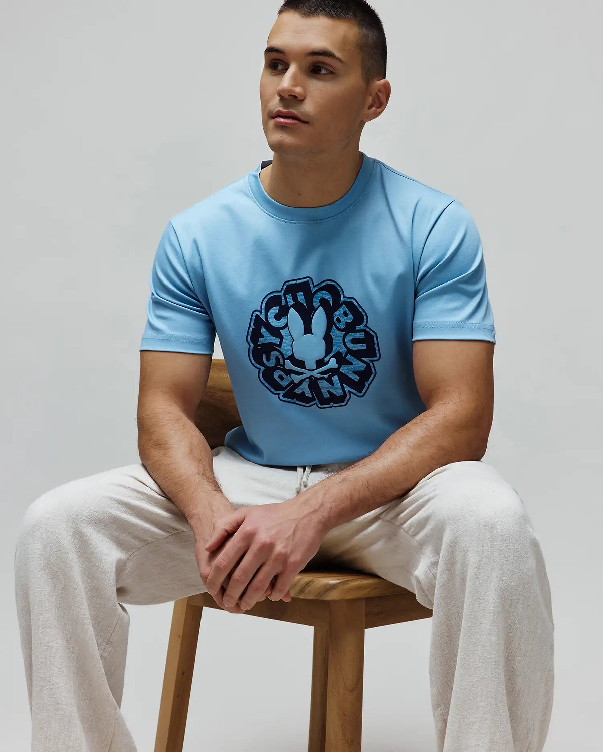 Mens Toby Graphic Tee in light blue, classic fit, smooth jersey knit, featuring a large dark blue circular Psycho Bunny skull logo and brand name graphic on the chest.