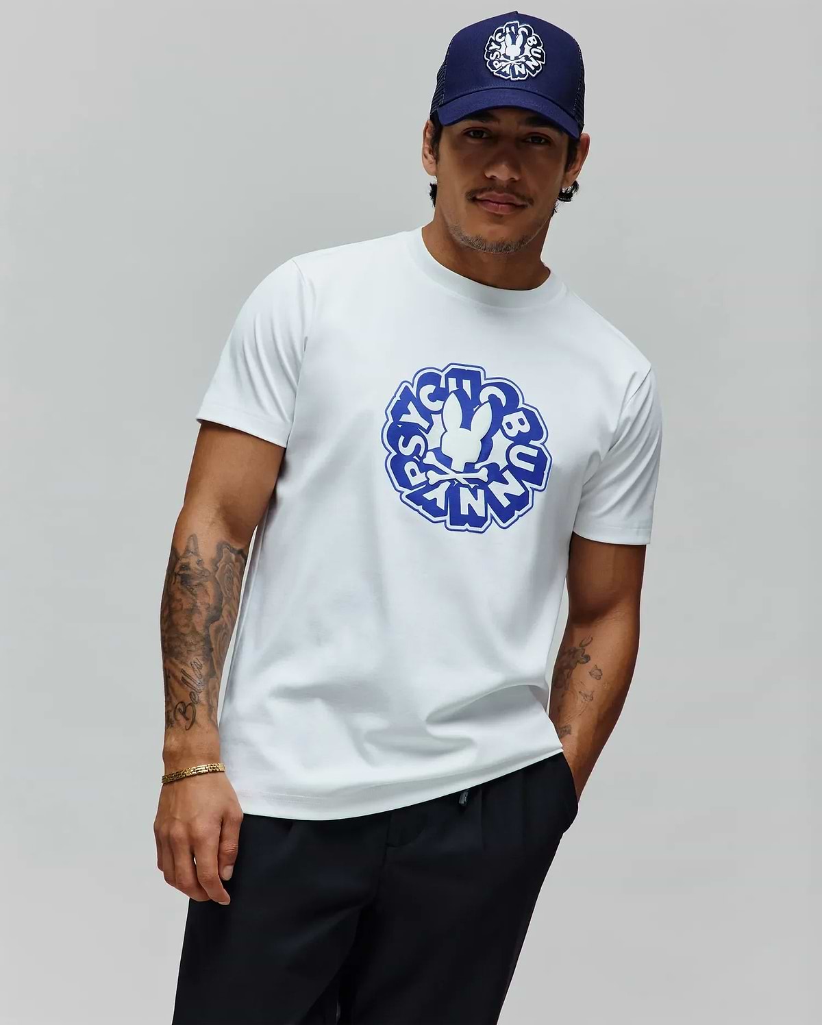 Mens Toby Graphic Tee, a classic fit white jersey t-shirt featuring a large central blue Psycho Bunny skull and crossbones logo within a circular graphic text design. (2)